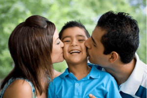 Both parents kissing son on the cheek